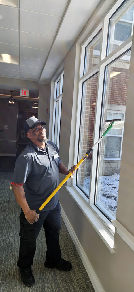 Worker washing windows on a high-rise senior community building using a long-handled squeegee.