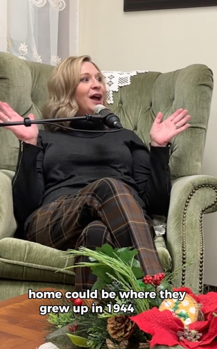 Elizabeth Thompson speaking into a microphone during a podcast recording, seated in a vintage green armchair with festive holiday decor nearby. Subtitles display: 'home could be where they grew up in 1944.