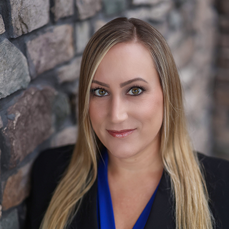 Professional headshot of Jessica Pope, Executive Director at Vitalia Solon, smiling in front of a stone wall background.