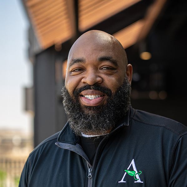 Thomas Drummer, Culinary Director at Vitalia Solon, smiles in an outdoor headshot taken under a shaded entrance, wearing a black jacket with the Arrow logo.