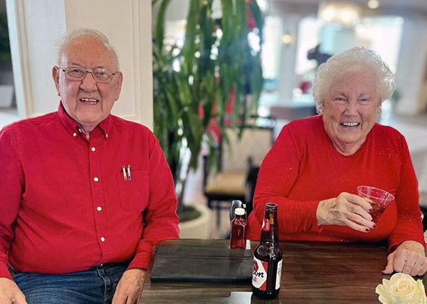 A senior man and woman both wearing bright red smile while sharing a dining table.