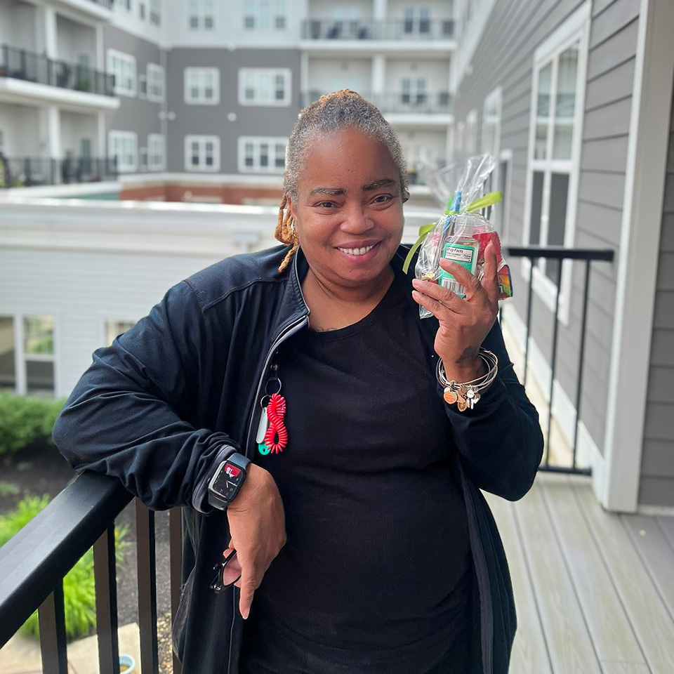 A team member smiles, the exterior of Vitalia Solon in the background, holding a gift bag.