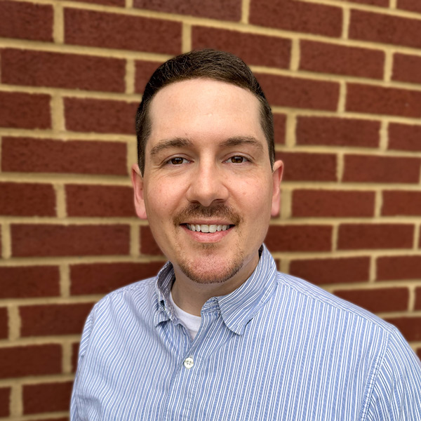 Kory Kerns, Business Office Director at Vitalia Solon, smiling in a professional headshot, wearing a blue striped button-down shirt, with a brick wall background.