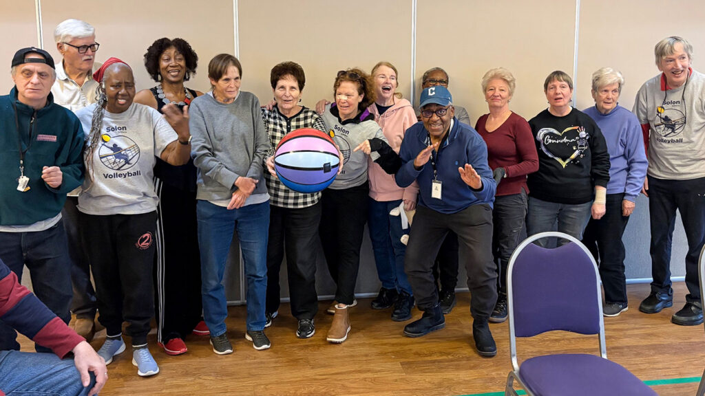 A group of residents and loved ones at Vitalia Solon smile, posing with a beachball used in beachball volleyball.