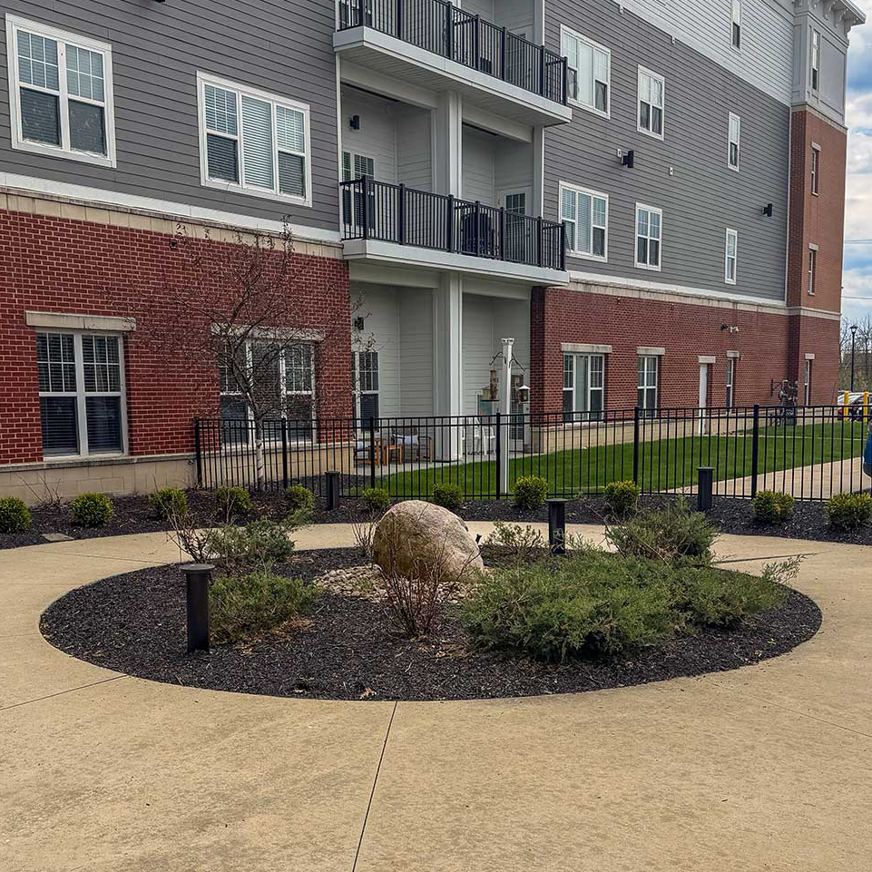 A circular mulch bed with circular sitting area, containing plants and a central stone.