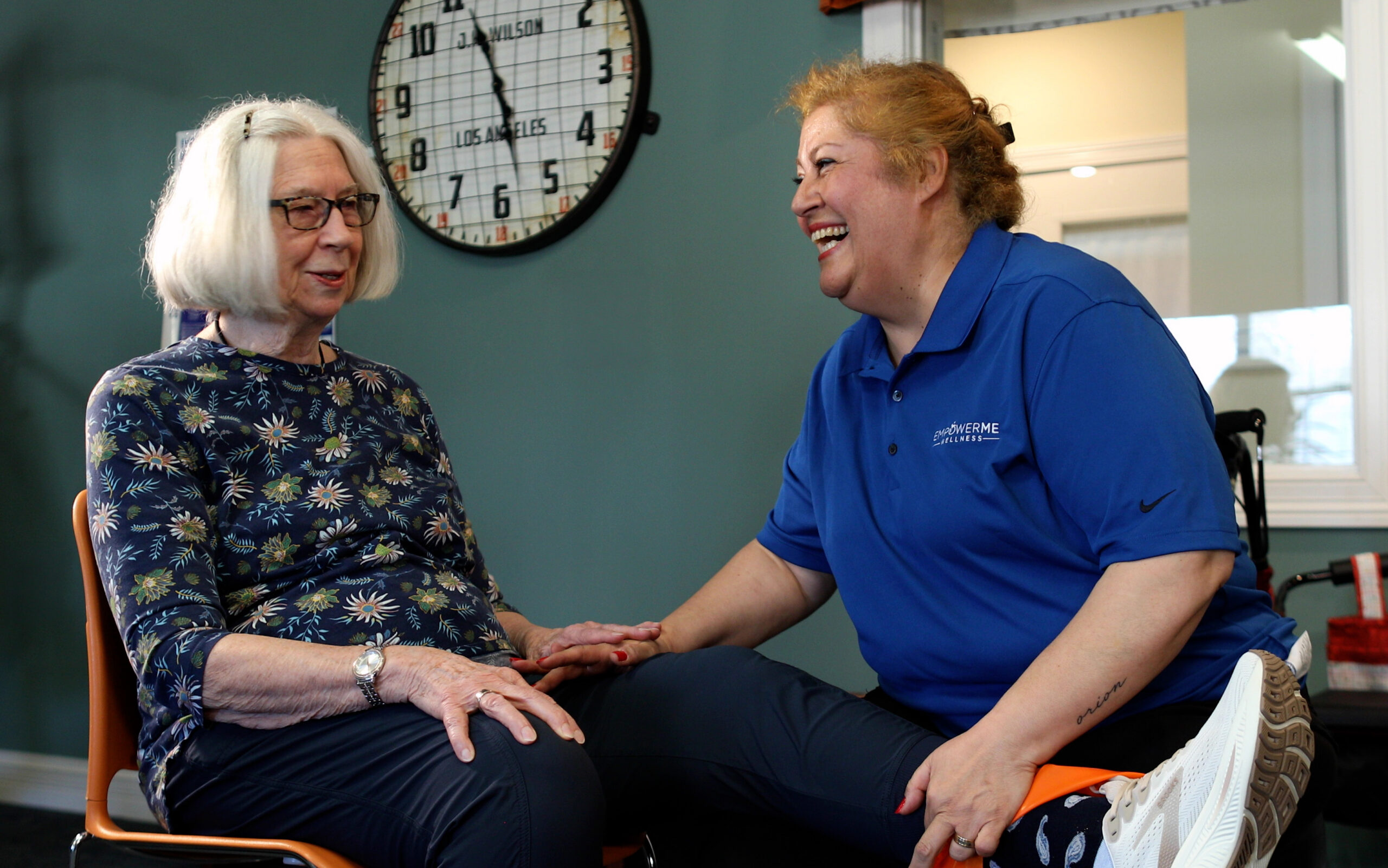 EmpowerMe Wellness team member laughs with a resident during a seated stretching or mobility session.